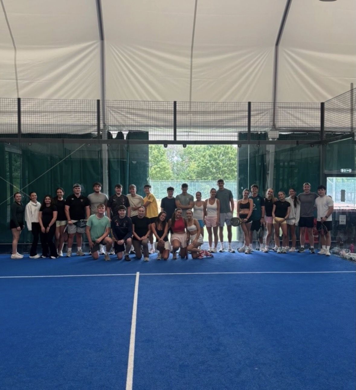Around thirty players lined up together on an indoor blue padel court