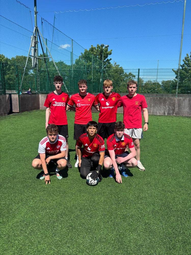 A team of seven in red jerseys posing on an astro pitch on a sunny day
